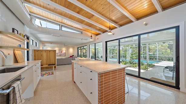 A modern kitchen with a large island, wooden ceiling beams, and a view of an outdoor pool. - Gorgeous Mid-Century Modern Pool Home on Private Canal, Mins to Siesta Key Beach (Siesta Key)
