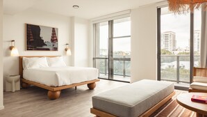 Un dormitorio moderno con una cama grande, un sofá más pequeño, una mesa redonda y un ventanal con vistas a la ciudad.
