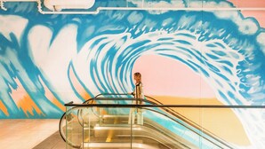 Un escalier mécanique dans un espace public, avec une fresque représentant une vague peinte sur le mur qui se trouve derrière.