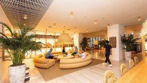 Un hall d’entrée moderne avec un espace salon aux lignes courbes, une grande plante et un comptoir d’accueil en bois.