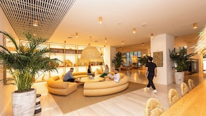 En modern entréhall med en böjd sittgrupp, en stor växt och en receptionsdisk i trä.