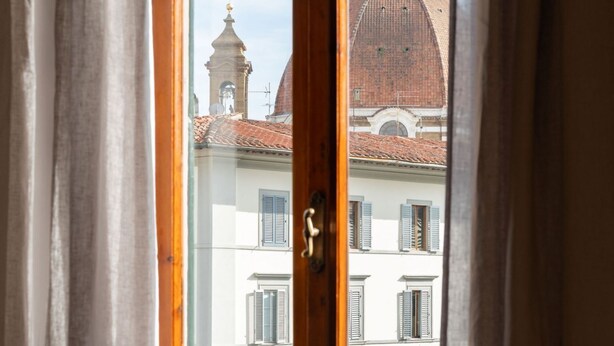 Vista per una finestra amb un marc de fusta, que mostra un edifici amb una cúpula i un campanar.
