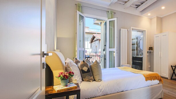 A bedroom with a bed, bedside table, and a window with curtains. - Fiesolana's Flower with balcony (Firenze)