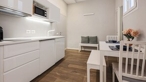 A compact kitchen with white cabinetry, a microwave, and a dining area with a white table and chairs. - Fiesolana's Flower with balcony (Firenze)