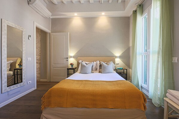 A bedroom with a bed, a mirror, a door, a nightstand, and a window with curtains.