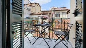 A balcony with a table and chairs, a flower vase, and a view of neighboring buildings. - Fiesolana's Flower with balcony (Firenze)