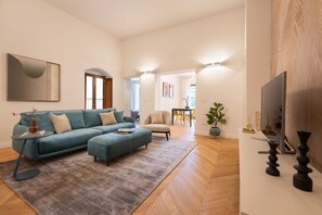 Un soggiorno con divano, poggiapiedi e televisore su un mobile.