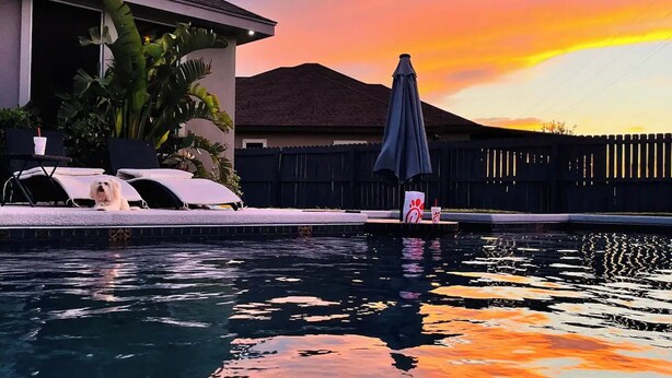 A swimming pool with a sunset view, a covered patio with lounge chairs, and a wooden fence. - Cozy stay in Mission - With Pool & Patio (Mission)