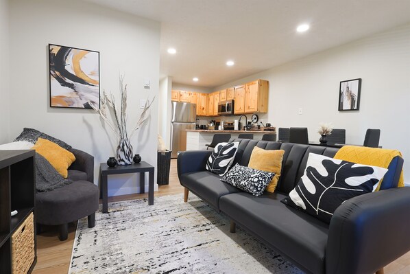 A modern living room with a sofa, coffee table, and a kitchen area in the background. - Luxuriously Contemporary Condo WL1401 | Powder Mtn (Eden)