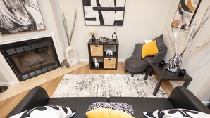 Een moderne woonkamer met een open haard, een zwart-wit bank met gele kussens, een bijzettafeltje en abstracte wanddecoratie.