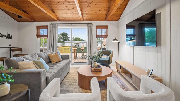 A modern living room with a wooden ceiling, a grey sofa set, a round coffee table, and a TV mounted on the wall. - 4br 3ba / 10 min to NRG / hot tub / sauna / firepit (Oak Hill)