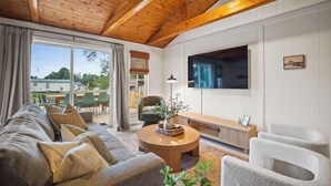 A cozy living room with a wooden ceiling, a large TV, a sofa, and a dining area with chairs and a table. - 4br 3ba / 10 min to NRG / hot tub / sauna / firepit (Oak Hill)