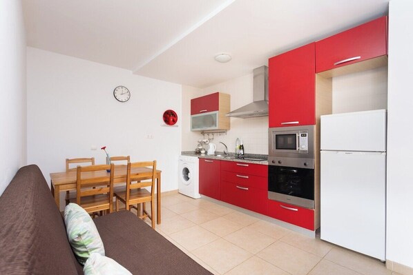 A compact kitchen with red cabinets, a microwave, a stove, and a refrigerator.
