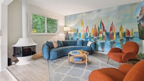 Ein modernes Wohnzimmer mit einer gebogenen, blauen Couch, einem weißen Kamin, einem farbenfrohen Wandgemälde mit Segelboot und orangefarbenen Sesseln.