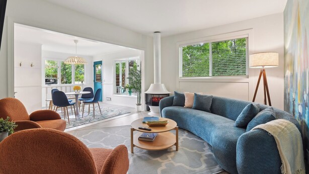 Ein modernes Wohnzimmer mit einem blauen Sofa, orangefarbenen Sessel und einem Essbereich mit Tisch und Stühlen.