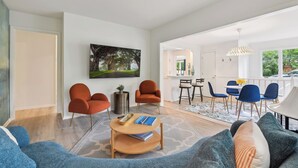 Ein modernes Wohnzimmer mit einer Couch, Sesseln, einem Couchtisch und einem Essbereich mit Stühlen und einem Tisch.