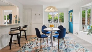 Ein Essbereich mit einem runden Tisch, vier blauen Stühlen, einem gemusterten Teppich und einer Pendelleuchte.