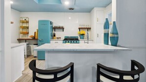 Eine moderne Küche mit einer zentralen Kochinsel, einem blauen Kühlschrank und einem Herd. Vor der Insel stehen zwei schwarze Stühle.