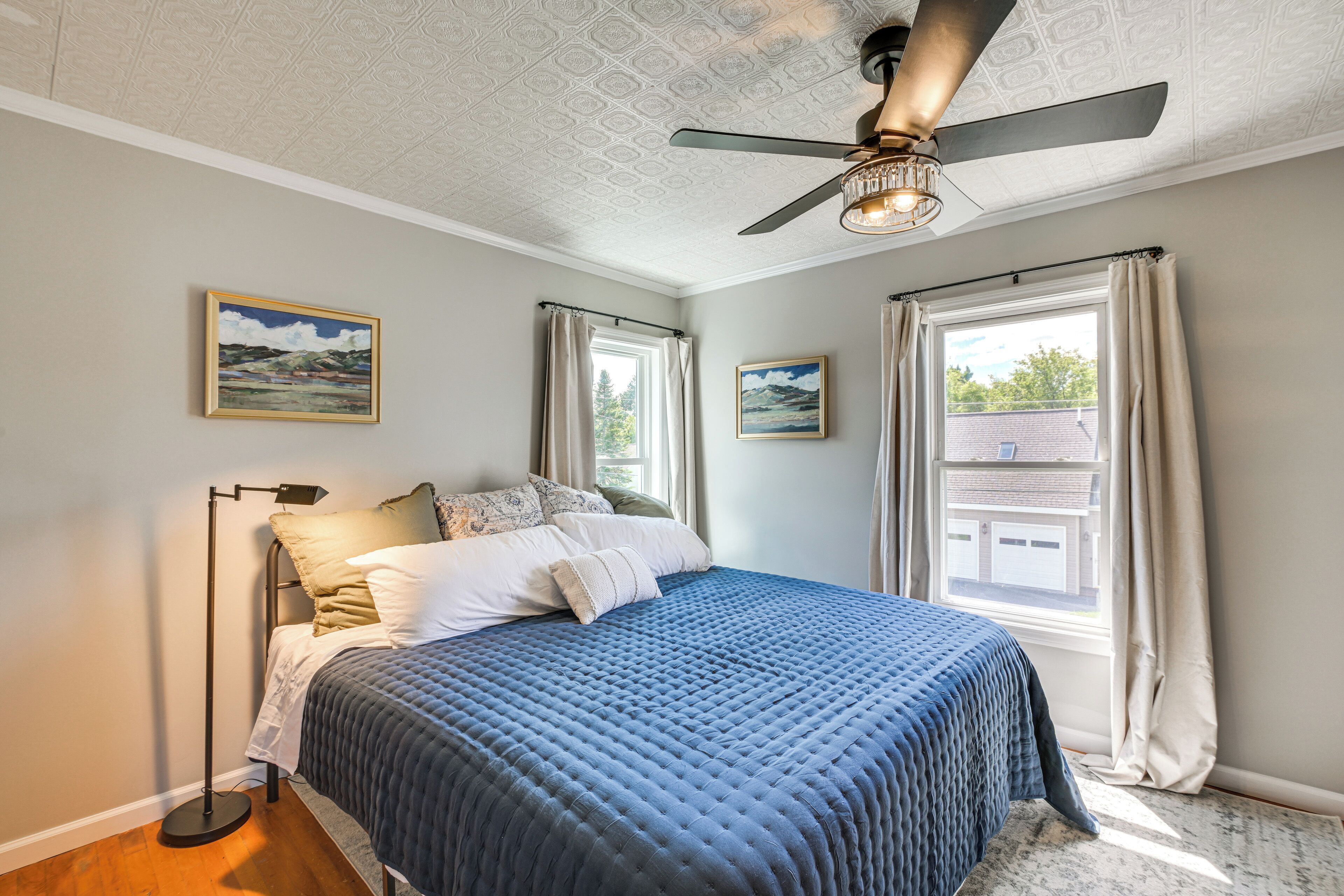 Ein Schlafzimmer mit einem Bett, Deckenventilator und zwei Fenstern mit Vorhängen.