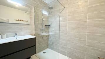 A modern bathroom with a glass shower enclosure, a white sink, and a dark vanity.
