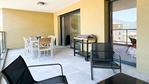 A balcony with a dining table and chairs, a small table with a chair, and a view of buildings and mountains. - BEL'ORIZONTE - Two rooms near the sea (T) (PROPRIANO)