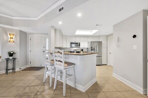 A modern kitchen with white cabinetry, a central island with bar stools, a microwave, and a refrigerator.