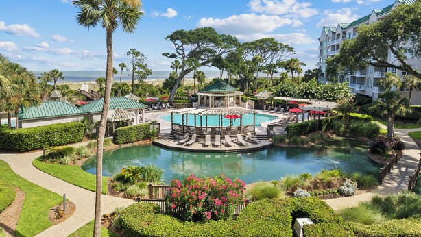 A resort with a central pool, lounge areas, and a view of the ocean. - 4205 Windsor @ Palmetto Dunes | Oceanfront Villa | Pool & Spa | Moments to Beach (Hilton Head Island)