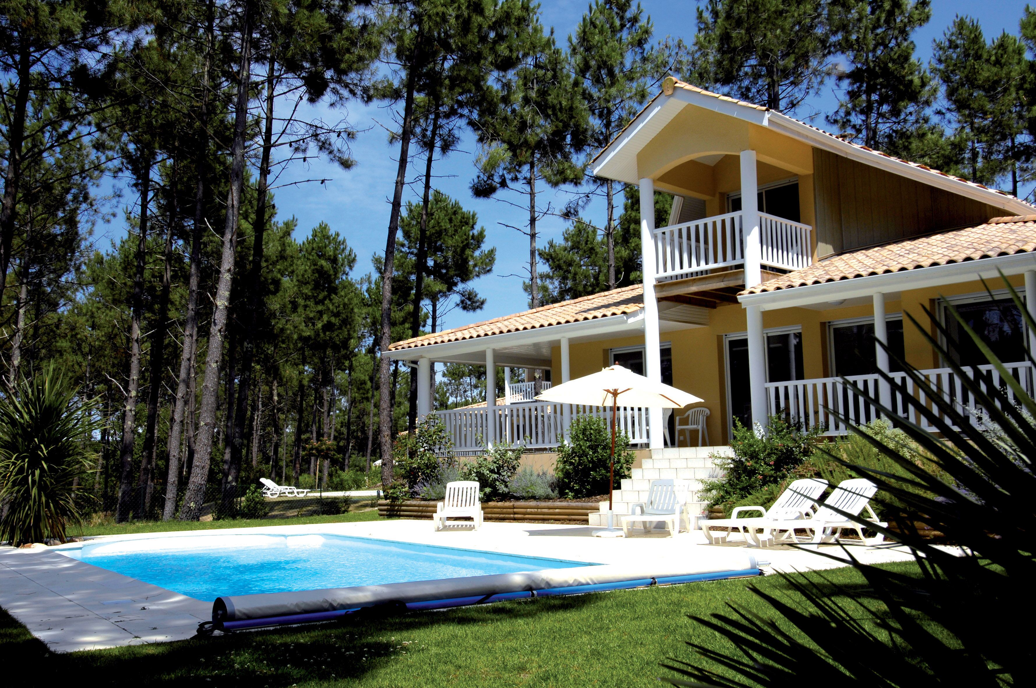 Una casa de dos pisos con balcón, piscina y césped con sillas de descanso.