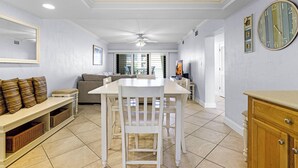 A dining area with a white table and chairs, a ceiling fan, and a clock on the wall. - Castle Reef 428 - Lovely location on No drive Beach (New Smyrna Beach)