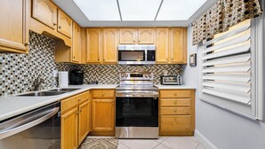 A kitchen with wooden cabinets, a microwave, an oven, and a dishwasher. - Castle Reef 428 - Lovely location on No drive Beach (New Smyrna Beach)