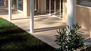 Un patio cubierto con techo de tejas rojas, columnas blancas y amplias puertas de vidrio.
