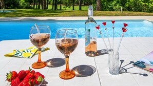 Une table placée au bord de la piscine, avec deux verres à vin, une bouteille et une assiette de fraises.