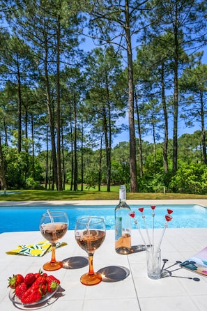 A poolside table with two wine glasses, a bottle, and a plate of strawberries.