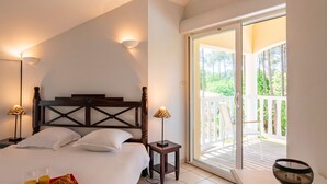 Une chambre avec un lit, des lampes de chevet, un plateau de petit-déjeuner, une chaise en bois, une table et un balcon donnant sur un paysage verdoyant.