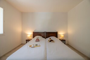 Una cama doble con cabecera de madera, dos mesitas de noche con lámparas, un oso de peluche, un mono de peluche y un libro sobre la cama.