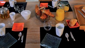 A breakfast table set with croissants, orange juice, and coffee, overlooking a wooden deck and a white picket fence. - À 3,5 km des plages de Lacanau | Villa + piscine (Lacanau​)
