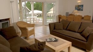 A living room with a brown sofa, wicker chairs, a wooden coffee table, and a television. - À 3,5 km des plages de Lacanau | Villa + piscine (Lacanau​)