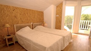 A room with two beds, wooden flooring, and a balcony with a railing. - À 3,5 km des plages de Lacanau | Villa + piscine (Lacanau​)
