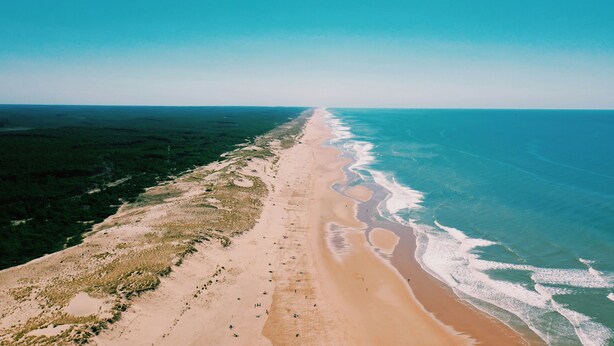 Vista aérea de una playa con una extensa franja de arena y océano.