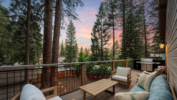 A deck with a wooden bench, two chairs, and a sofa, surrounded by tall trees and a sunset view. - One Block to Beach, Restaurants, Bars, Brewery. Modern mountain luxury. (Kings Beach)