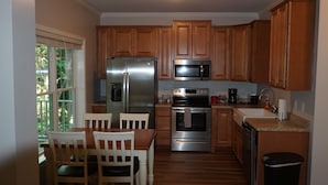 Cocina compacta con armarios de madera, electrodomésticos de acero inoxidable y una zona de comedor con mesa y sillas.