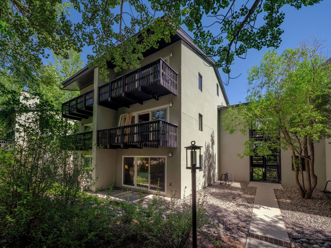 A modern two-story building with balconies, a covered entrance, and a pathway leading to the door.