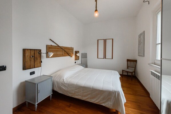 Un dormitorio con cabecera de madera, una cama, un pequeño armario, una silla y un radiador.