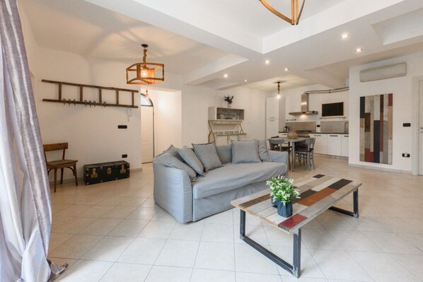 A spacious living area with a sofa, a coffee table, a dining table, and a kitchen in the background.