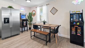 A compact kitchen with a refrigerator, a small dining table with chairs, a bench, and a neon sign. - Walkable Gem : Retro Arcades : Near Lauderdale-by-the-Sea (Fort Lauderdale)