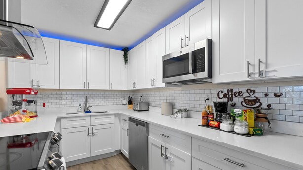 A modern kitchen with white cabinets, a stainless steel microwave, and a coffee-themed backsplash. - Walkable Gem : Retro Arcades : Near Lauderdale-by-the-Sea (Fort Lauderdale)