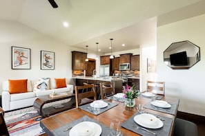 Cocina moderna con armarios de madera, una isla central y un comedor con mesa de madera dispuesta para cuatro comensales.