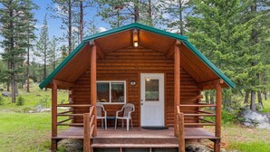 A wooden cabin with a porch, two chairs, and a door.
