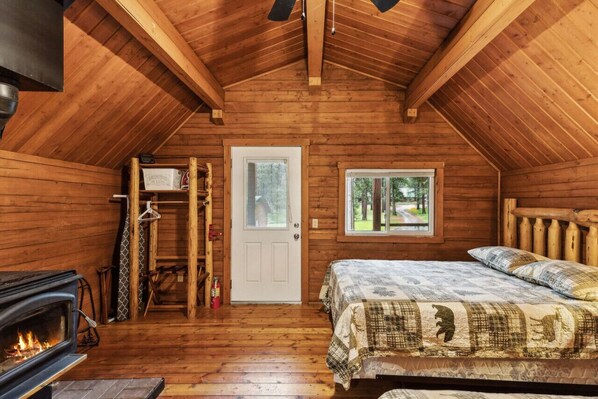 Un chalet confortable avec un intérieur en bois, une cheminée, un lit recouvert d’une courtepointe et une fenêtre donnant sur le paysage extérieur.