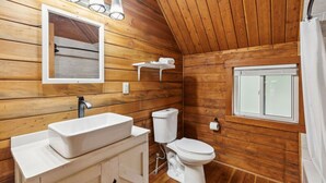 Ein Badezimmer einer Holzhütte mit Waschbecken, Toilette und Spiegel, alles in Weiß.
